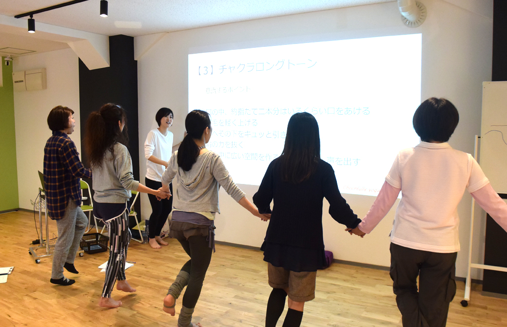 高橋淳子先生の声かけ、はないちもんめのように手をつないで横一列になった生徒さんが壁に向かって発声している様子