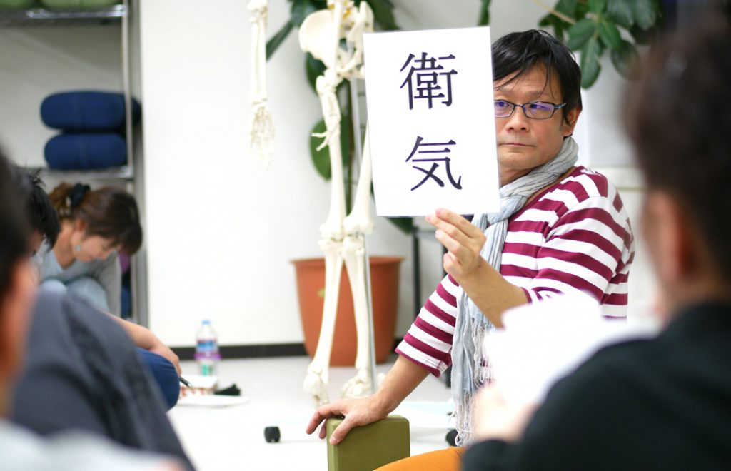 経絡ワークショップの講座風景。講師（内田かつのり）が衛気（えき）の資料を生徒に見せている様子