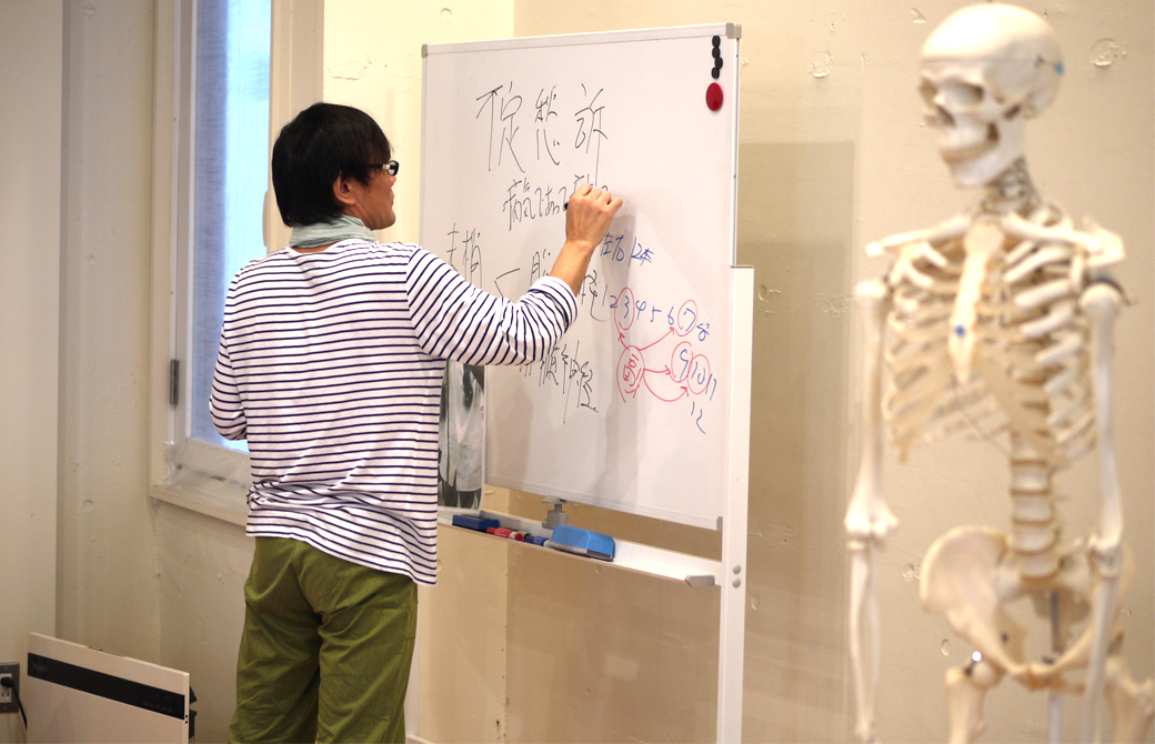 ヨガ×東洋医学の講座風景。講師内田かつのりがホワイトボードに板書している。