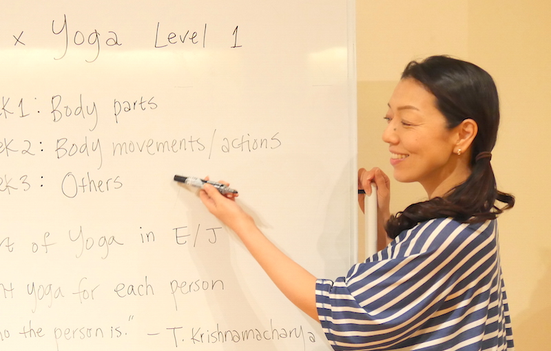ホワイトボード前でヨガ英語の表現方法について説明している川原朋子先生