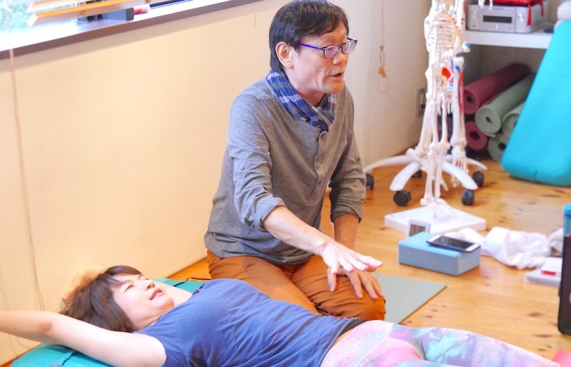 仰向けになって壁に手を伸ばしている生徒さんとその横で説明している内田先生