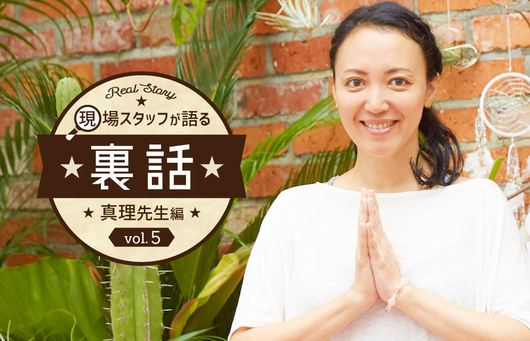 レンガの壁と植物の前で笑顔合掌している真理先生