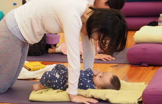 赤ちゃんをブランケットの上に寝かせて四つん這いで見つめるお母さん：産後ヨガクラス