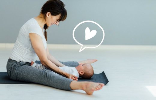 ヨガマットの上に足を開いて座り、赤ちゃんをその間に寝かせる女性