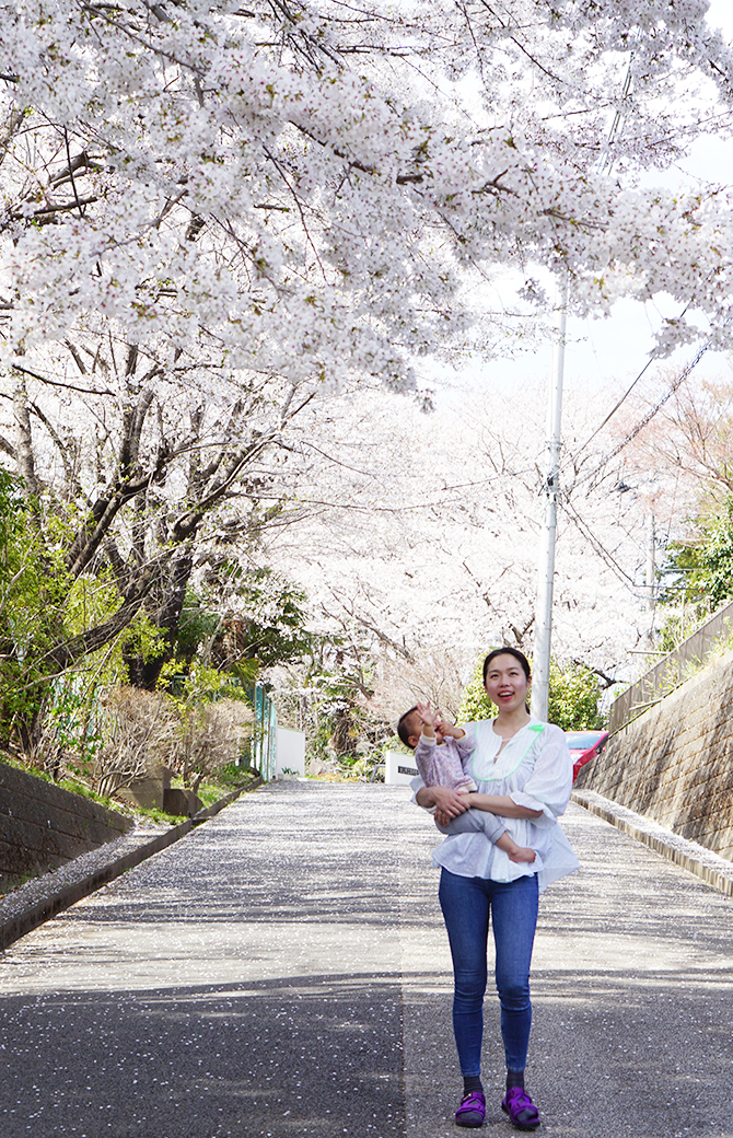 佐久間涼子先生が娘さんをだっこして桜の木の下に立っている