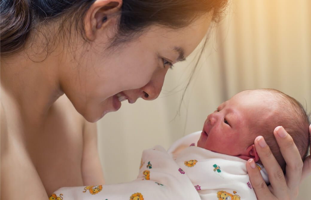 小さな新生児を抱いて微笑む母親