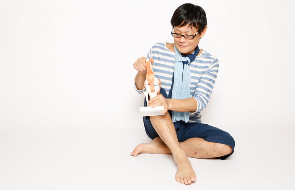 内田かつのり先生が膝の模型を持って座っている