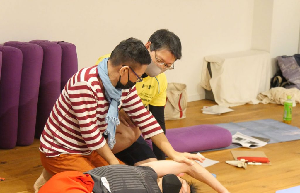 横になる生徒さんに手技をする内田かつのり先生と横で見ている生徒さん