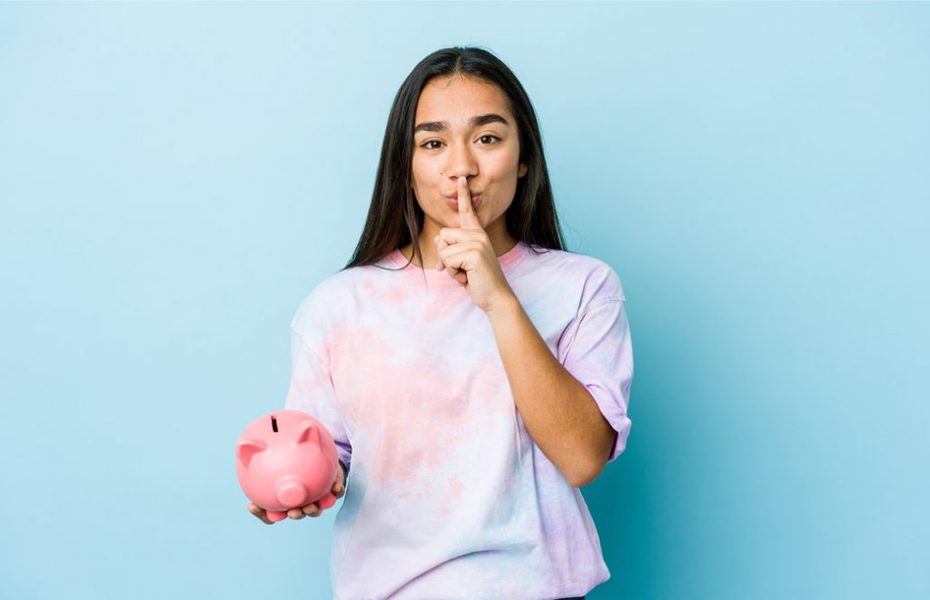 長い髪の女性。豚の貯金箱を持ち、口に指をあてている