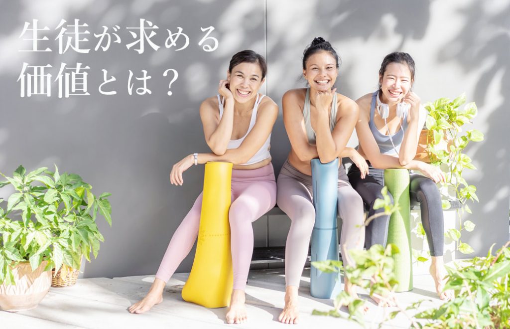 木陰のベンチに丸めたヨガマットをもって座った3人の笑顔の女性。周りには観葉植物の植木鉢。右上に白文字で「生徒が求める価値とは」