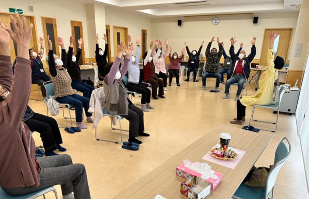 椅子に座って手を上げるポーズをしているたくさんの参加者